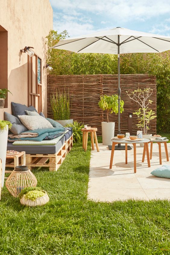 a small rustic summer terrace with a tiled space, a pallet sofa, wooden stools and potted greenery and candle lanterns