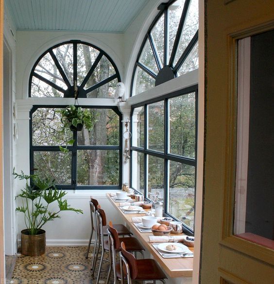 a small sunroom turned into a meal space, with a windowsill table and potted greenery