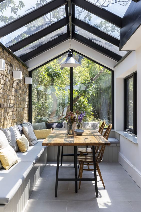 a small sunroom with a dining space, wall and pendant lamps, with a large L-shaped bench and a dining table