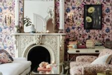 a sophisticated living room with pink floral wallpaper, a creamy sofa, a pink floral chair, a coffee table, a fireplace and a chandelier