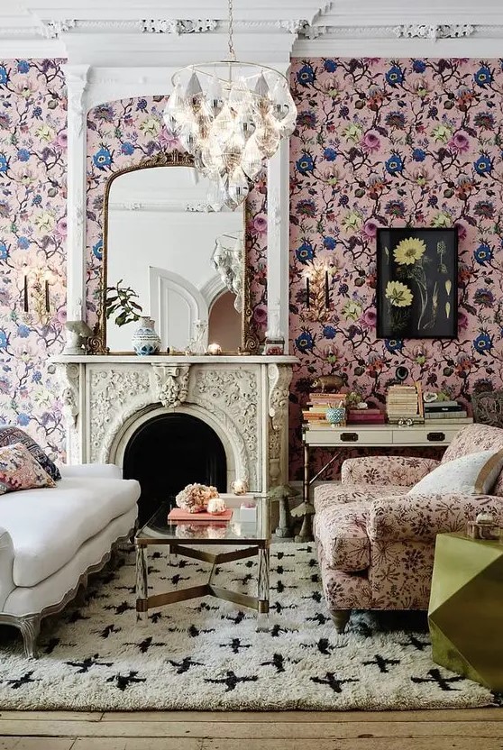 a sophisticated living room with pink floral wallpaper, a creamy sofa, a pink floral chair, a coffee table, a fireplace and a chandelier