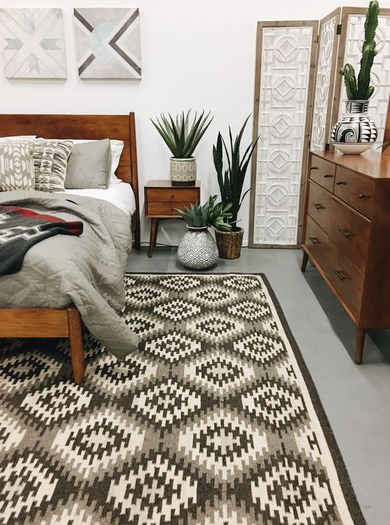 a stylish mid-century modern bedroom with a geometric rug, rich-stained furniture, potted greenery and artworks