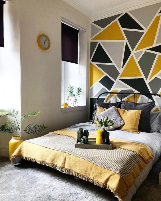 a tiny bedroom with a grey, black and yellow geometric accent wall, a black metal bed with matching in color bedding