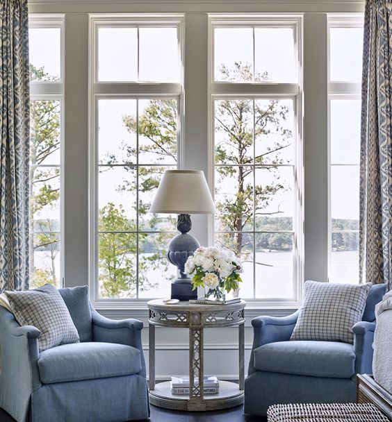 a vintage coastal sunroom with blue furniture and a lamp, a woven chest, an elegant table and printed curtains a vintage coastal sunroom with blue furniture and a lamp, a woven chest, an elegant table and printed curtains