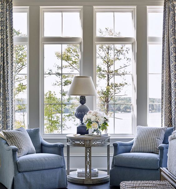 a vintage coastal sunroom with blue furniture and a lamp, a woven chest, an elegant table and printed curtains