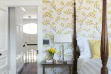 a vintage-inspired bedroom with yellow floral walls, a heavy bed with pillars, a chair and nightstands plus blooms
