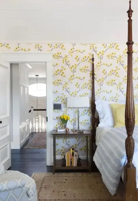 a vintage inspired bedroom with yellow floral walls, a heavy bed with pillars, a chair and nightstands plus blooms
