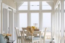 a vintage-inspired coastal sunroom with white and black vintage furniture, ligth blue upholstery, chic sea views