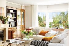 a vivacious living room with stained bookcases, coffee tables, white sofas, yellow pillows and geo printed textules, a view of the garden