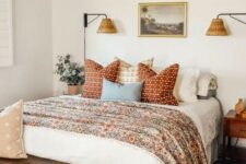 a welcoming bedroom in neutrals with a bed with floral and other printed bedding, a stained bench, a chandelier, stained nightstands