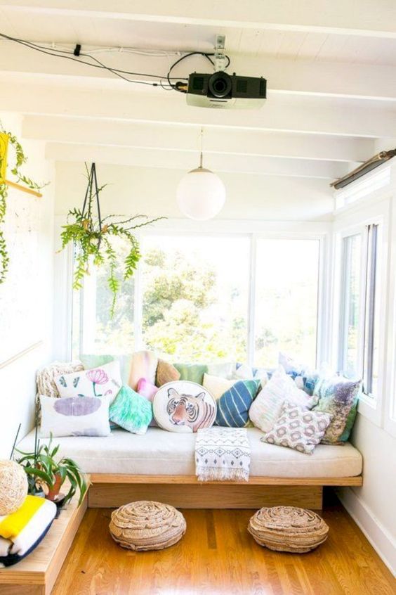 a welcoming sunroom with a sofa and lots of pillows, with footrests and potted greenery