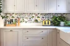 a white kitchen accented with a bright floral wallpaper backsplash, white countertops and potted plants plus a bold polka dot rug