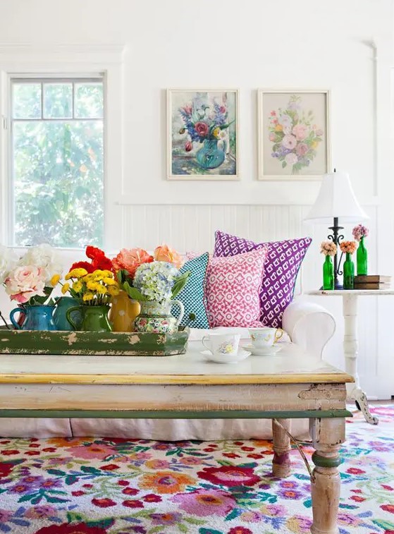 a white living room with a bold floral rug that makes a statement, a white sofa, floral artwork and blooms in vases