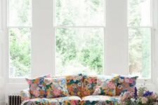 an airy living room with large windows, a floral sofa and a footrest, a pink chair, a coffee table and a crystal chandelier