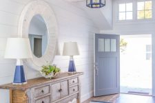 an amazing coastal entryway with white planked walls, a blue and grey striped rug, a wooden console table and blue touches