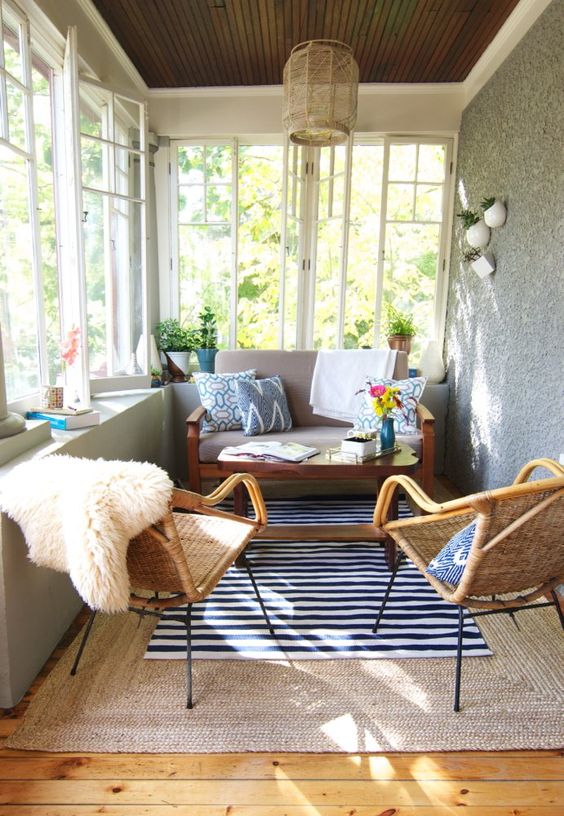 an eclectic and boho sunroom with wicker chairs and lamps, with layered rugs and touches of color