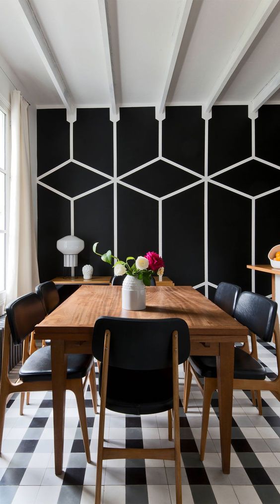 an elegant black and white dining space with a geo printed wall, a stained dining table, black chairs, a checked rug and some white touches