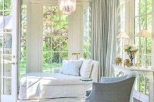 an elegant vintage sunroom with a white daybed and a light blue chair, a vintage table with lamps and a cool pendant lamp