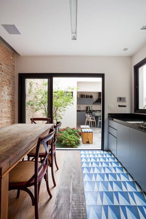 an indoor-outdoor kitchen with sleek grey cabinets and black countertops, a blue and navy geo tile floor and a dining zone with wooden furniture
