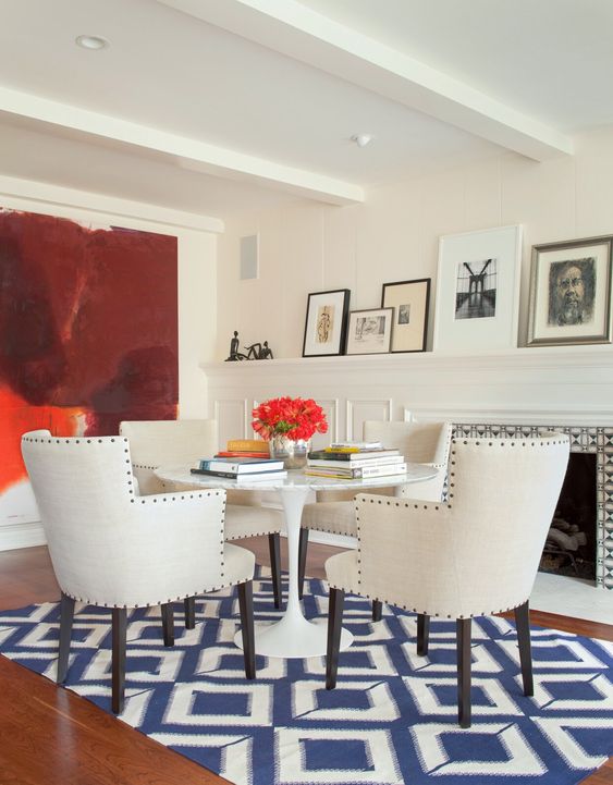 creamy wall panels, a non-working fireplace, a round table and creamy chairs, a navy and white geo printed rug and a bold artwork on the wall