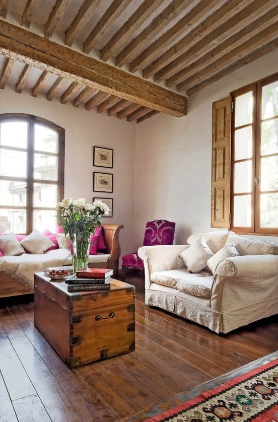a Provence living room with wooden beams and shutters, neutral refined furniture, a chest in the center and a gallery wall