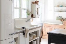 a beautiful vintage kitchen with white and stained cabinets, a black vintage table as a kitchen island, potted plants and pendant lamps and sconces