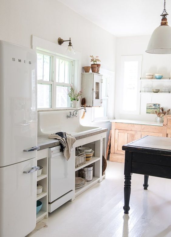 a beautiful vintage kitchen with white and stained cabinets, a black vintage table as a kitchen island, potted plants and pendant lamps and sconces