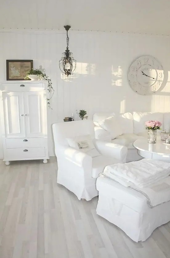 a beautiful white shabby chic living room with stylish vintage furniture, a clock, a chandelier and greenery in pots