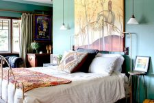a bold and whimsy vintage bedroom with green walls, a metal bed, colorful bedding, bold artworks and a stained glass chandelier