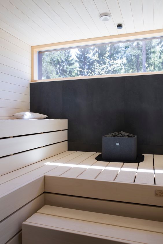 a bold steam room with a black wall, a skylight and bleached wooden benches is super modern