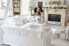 a catchy shabby chic living room in white, with a tan fireplace, vintage chandeliers, a mirror and lace curtains