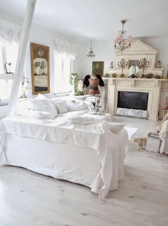 a catchy shabby chic living room in white, with a tan fireplace, vintage chandeliers, a mirror and lace curtains