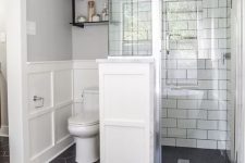 a chic bathroom with a black hex tiles floor, white subway tiles in the shower space and white paneling on the wall