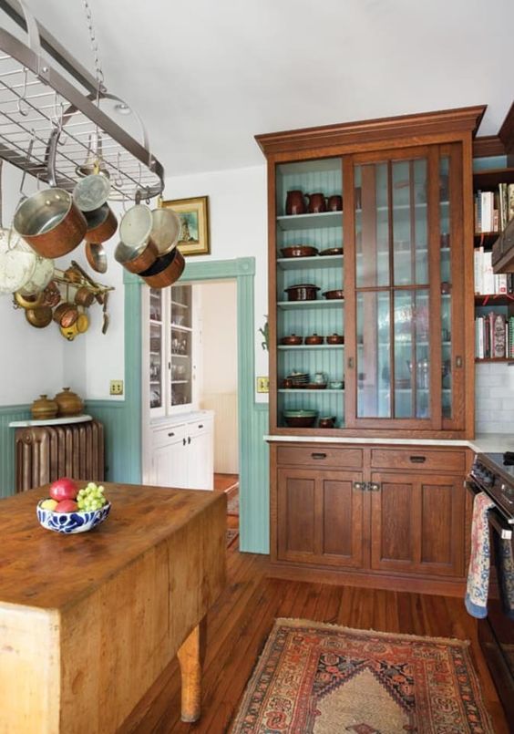 a chic vintage kitchen with mint green paneling, stained vintage furniture, a foldign table as a kitchen island, a hanger with pans