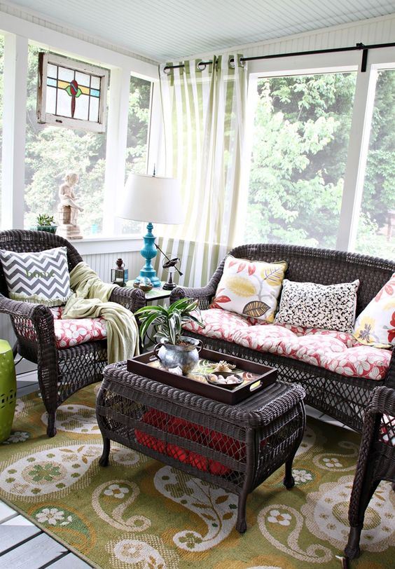 a chic vintage sunroom with dark rattan furniture, colorful textiles, a bright artwork and a blue table lamp