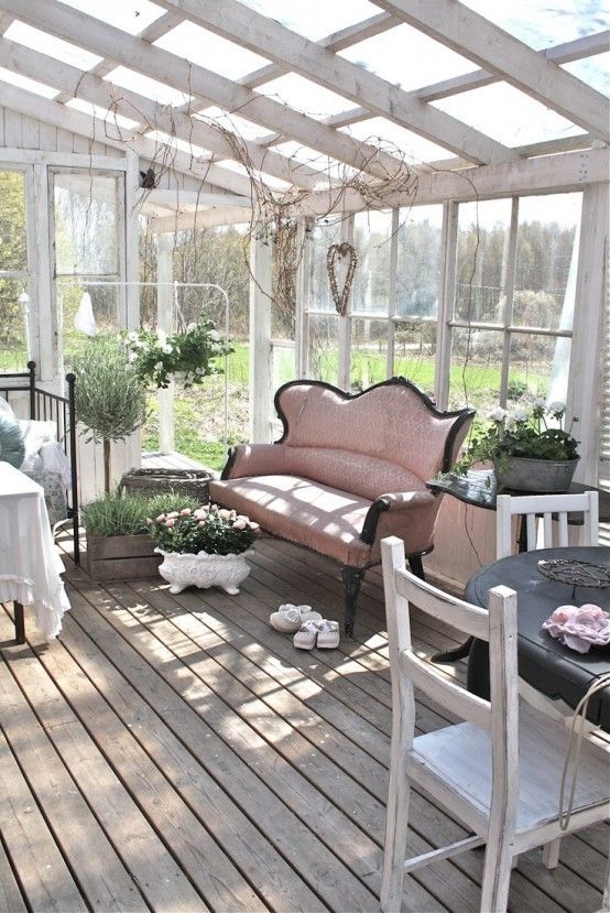 a chic vintage sunroom with neutral forged and wooden furniture, a pink sofa, potted blooms and much sunlight