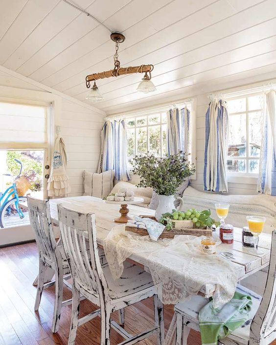 a chic vintage to shabby chic sunroom with white shabby furniture, striped curtains, greenery and a rustic lamp