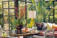 a colorful vintage sunroom with a dark stained table, refined chairs, a daybed with vibrant pillows, potted greenery and a gorgeous floral chandelier