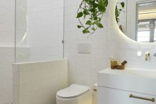 a contemporary bathroom clad with mosaic tiles, with a floating vanity, a half wall with glass to separate the shower space and a potted plant