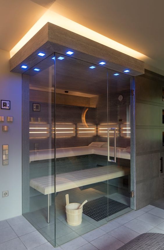 a cool modern sauna clad with dark stone and light-colored wood, with a couple of benches and built-in lights