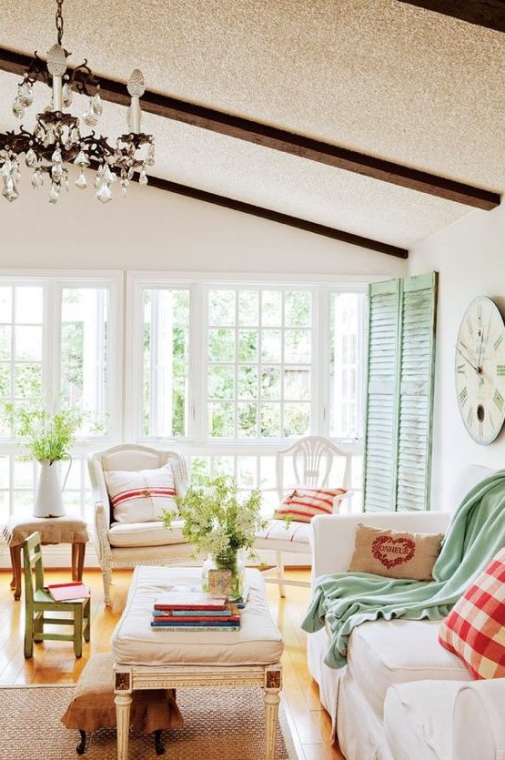 a cottage Provence with green shutters, neutral furniture, plaid and green textiles, a crystal chandelier and a jute rug
