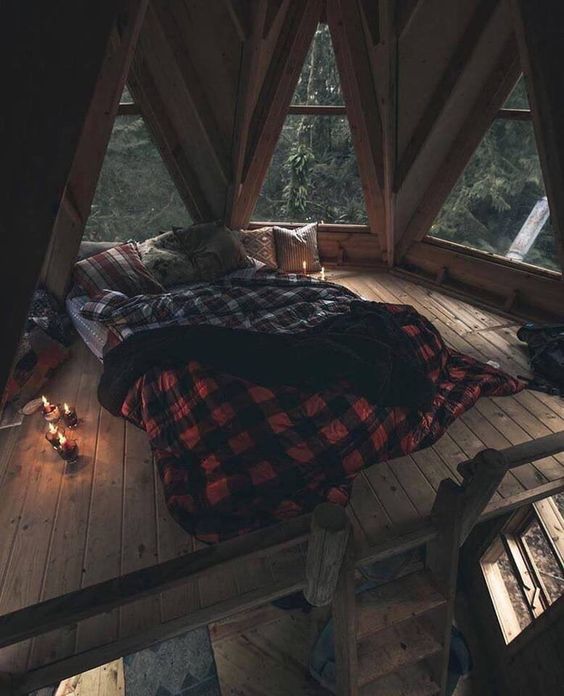 a cozy loft bedroom surrounded with uniquely shaped windows, with a low bed and only candles around
