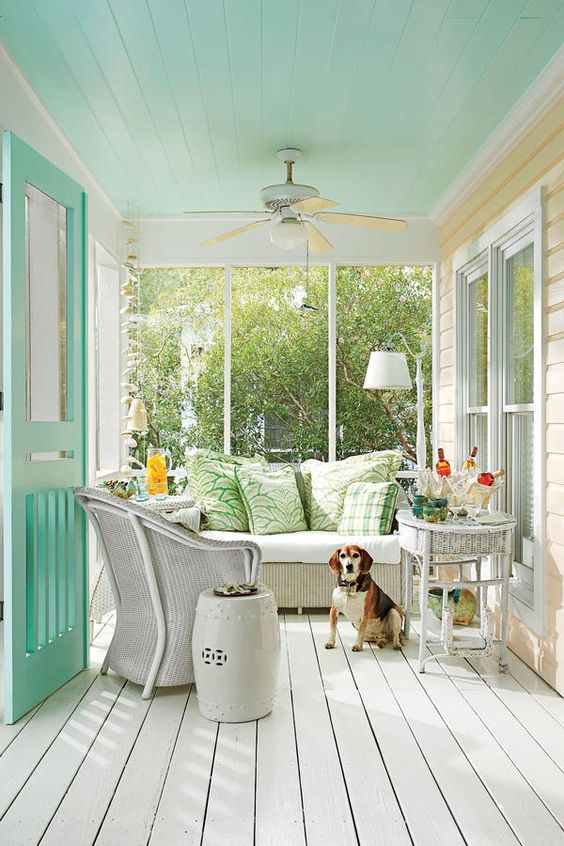 a cute neutral vintage sunroom with a mint ceiling, white wicker furniture, printed pillows and a minty door