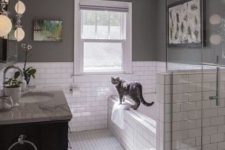 a farmhouse bathroom with white subway tiles and hex ones, with grey walls, a shower space with a pony wall and a black vanity