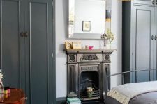 a laconic vintage bedroom in grey and white, with a fireplace, a pendant lamp with fringe and a metal bed