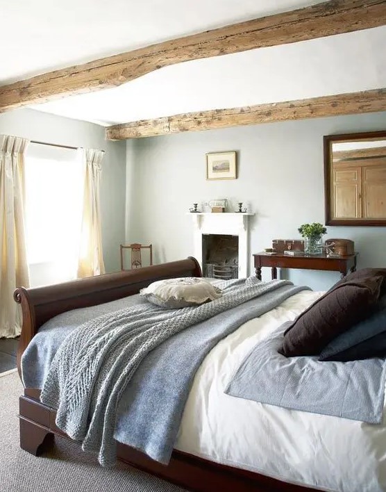 a lovely Provence bedroom with wooden beams, a fireplace, a dark stained bed and a mirror plus some vintage furniture