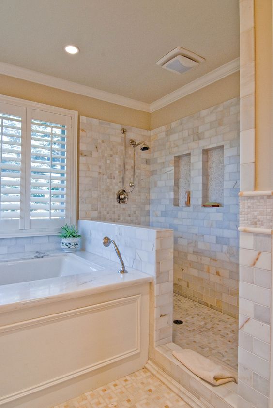 a lovely bathroom clad with marble tiles, with a half wall in the shower space, a bathtub clad with panels