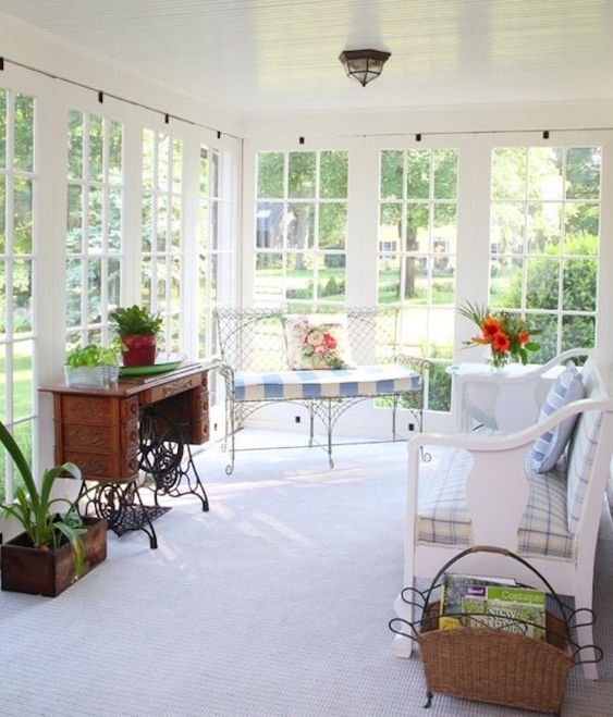 a lovely vintage sunroom with wooden and forged furniture, printed upholstery, potted greenery and blooms