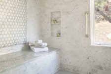 a luxurious white marble tile steam room with two long benches, niches and a window to enjoy the views