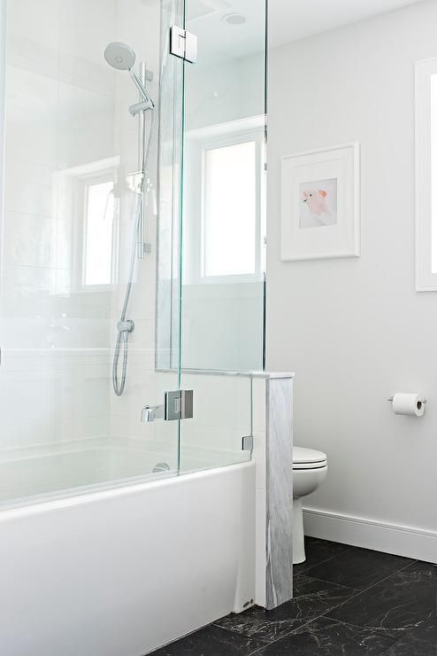 a minimalist bathroom with a black floor, a half wall that separates the toielt from the rest of the space, a shower-bathtub space